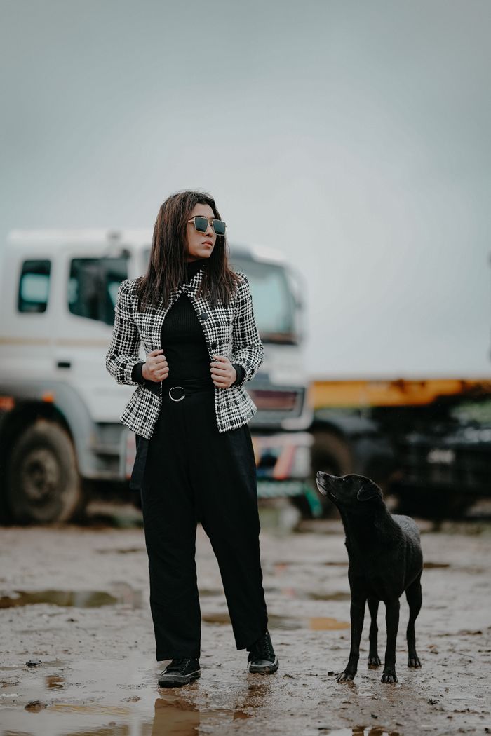 Fashionable woman and black dog standing outdoors with truck in the background.
