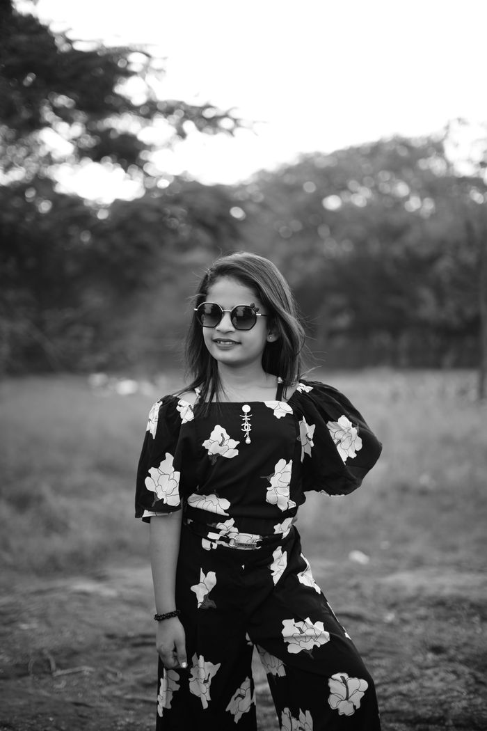 Stylish girl in floral outfit and sunglasses poses confidently outdoors.