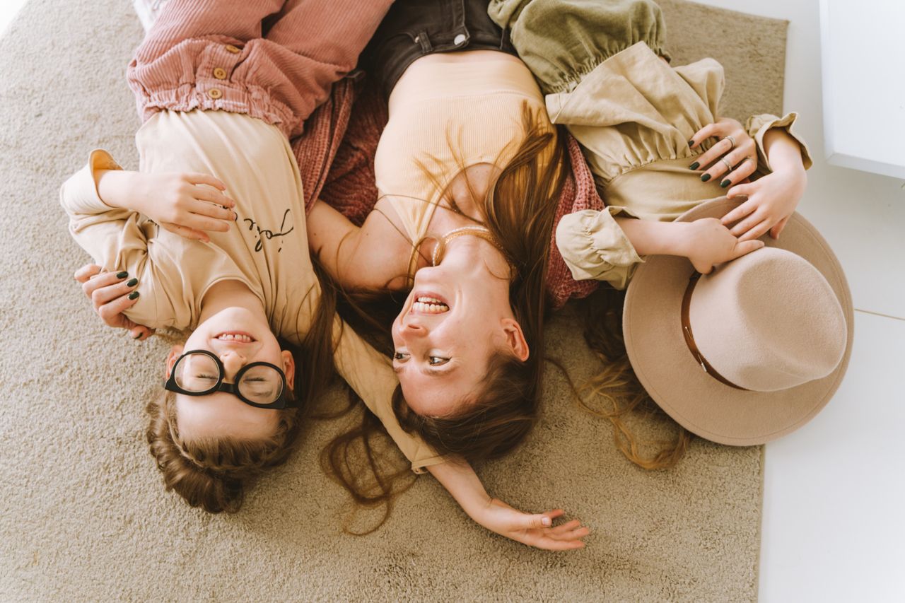 Mother and daughters lying happily on the carpet, embracing and smiling.